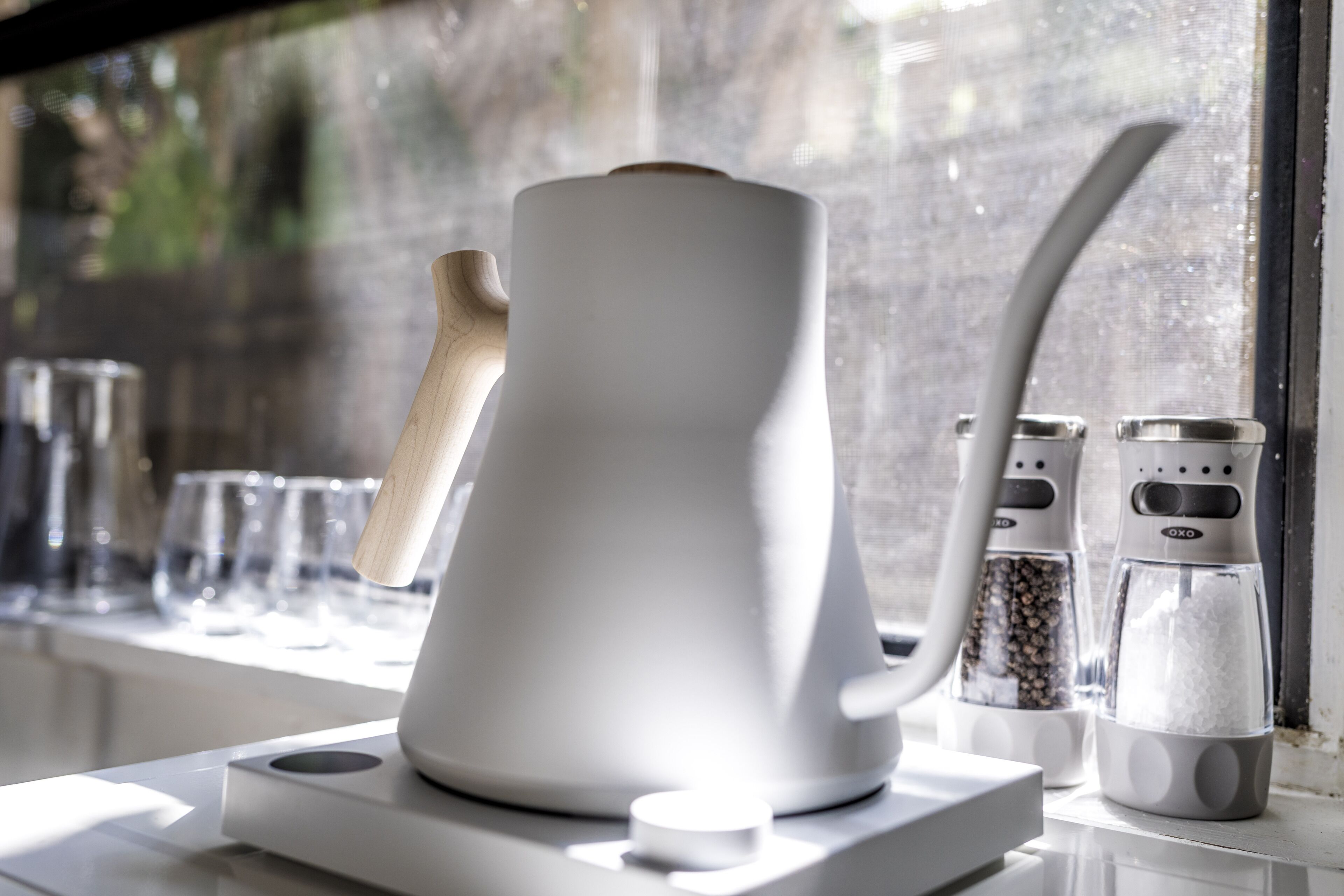 A modern kitchen with a unique coffee machine, salt and pepper shakers, and a window with a view of trees.
