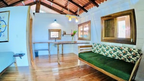Une pièce chaleureuse avec un plancher en bois, un canapé vert, un banc en bois, une petite table et une fenêtre avec des cadres en bois.