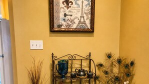 A hallway with a decorative metal rack holding kitchenware, a framed picture of the Eiffel Tower, and a vase with dried plants. - Relax in our beautiful New Orleans themed townhome

 (Ponchatoula)