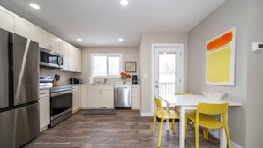 A modern kitchen with stainless steel appliances, a dining area with yellow chairs, and a view of the outdoors. - NEW - Euro-Style Suite - Whyte Ave/Clean/A/C/NFLX/Sleeps6
 (Edmonton)