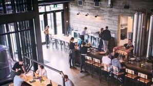A modern restaurant with high tables and chairs, large windows, and a bar area. - NEW - Euro-Style Suite - Whyte Ave/Clean/A/C/NFLX/Sleeps6
 (Edmonton)