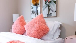 A bedroom with a bed, two pink fluffy pillows, white bedding, and two wall-mounted lamps. - NEW - Euro-Style Suite - Whyte Ave/Clean/A/C/NFLX/Sleeps6
 (Edmonton)