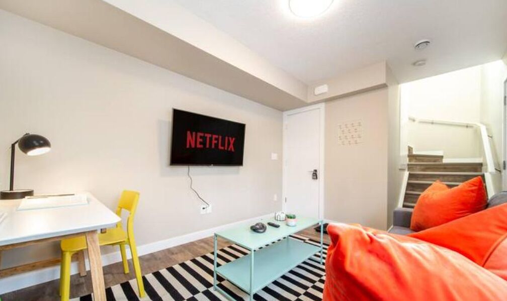 Una sala de estar moderna con un televisor de pantalla plana montado en la pared, una mesita, una silla amarilla y un sofá rojo.