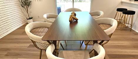 A dining area with a wooden table surrounded by six chairs with cushioned seats and metal frames.