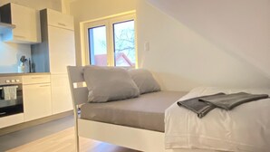 Habitación compacta y moderna con cama tipo altillo, una kitchenette pequeña y un amplio ventanal que proporciona luz natural.