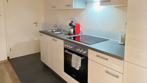 Una cocina moderna con un lavamanos de acero inoxidable, un hervidor rojo y un horno empotrado.