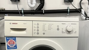 Una lavadora Bosch con un panel de control, un adhesivo que dice 'Mit Garantie' y una manguera conectada a la pared.