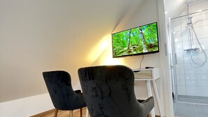 Una sala de estar moderna con un televisor de pantalla plana montado en la pared, dos sillas oscuras con patas de madera y suelo de madera.