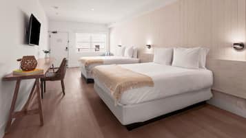 Une chambre d’hôtel moderne avec deux lits, un plancher en bois, un bureau avec une chaise et un téléviseur fixé au mur.