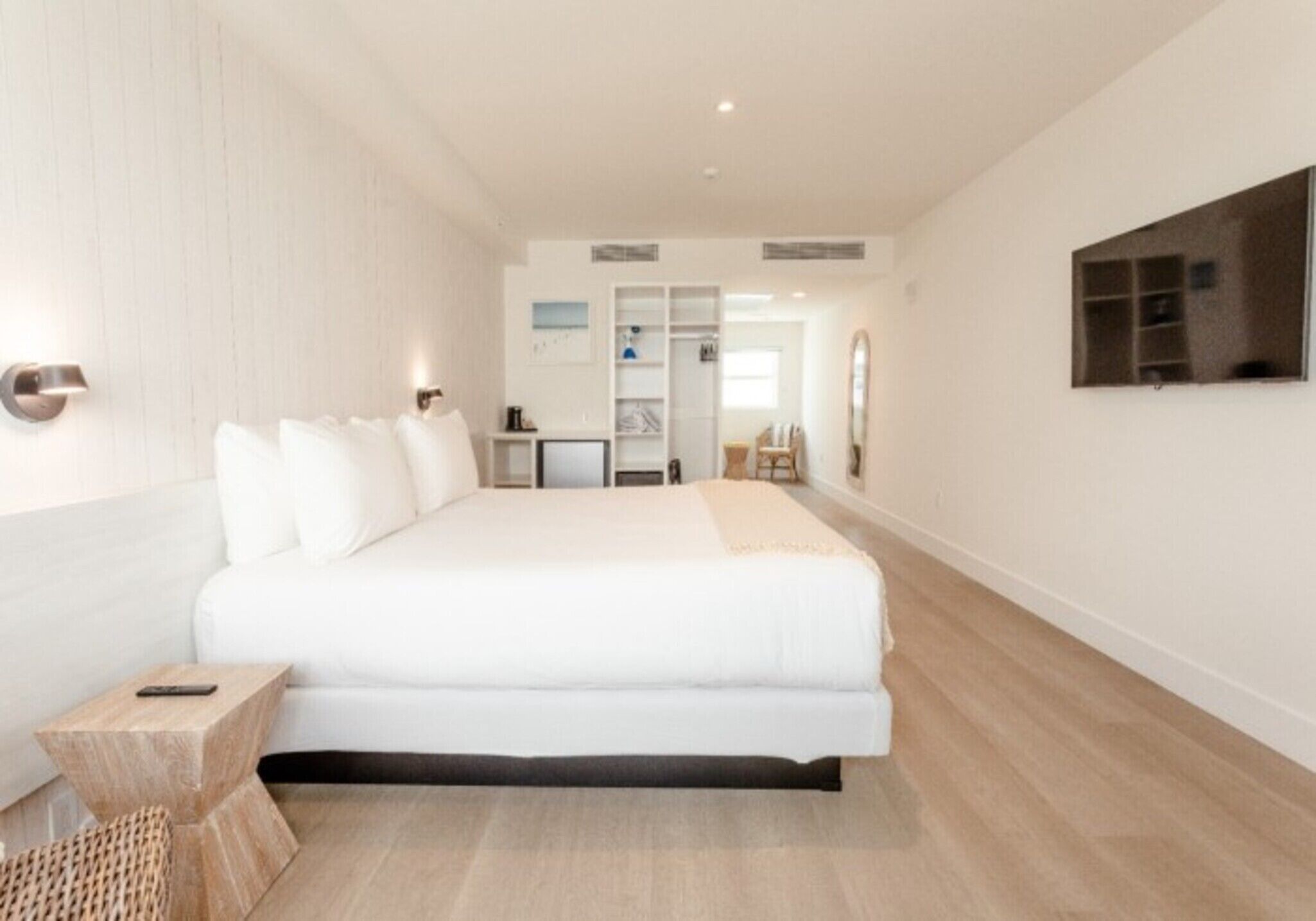 Un dormitorio moderno con una cama grande, mesitas de noche, una pequeña zona de estar y un televisor montado en la pared.