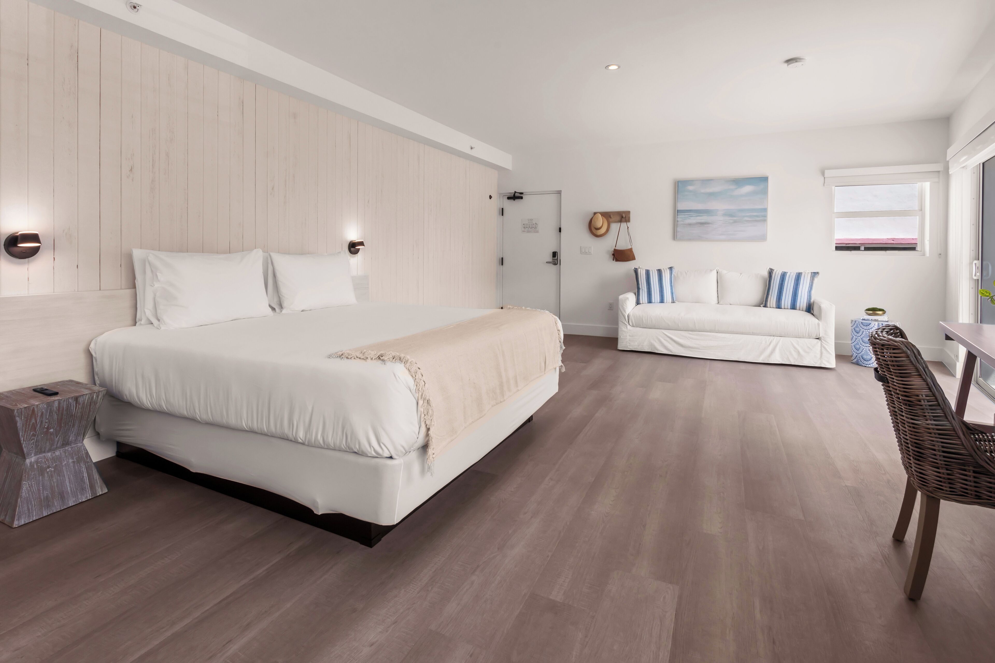A modern bedroom with a large bed, a smaller bed, a sofa, and a wicker chair.