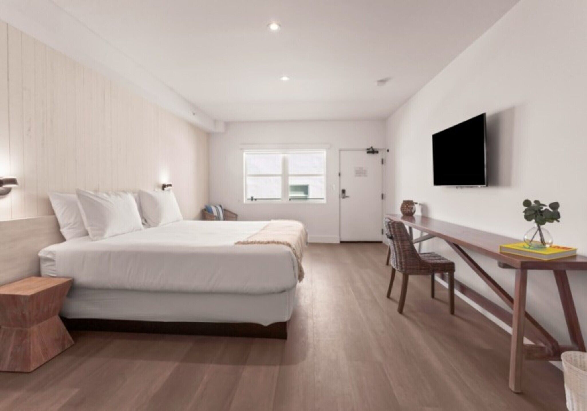 Un dormitorio moderno con cama, mesita de noche, silla y televisor montado en la pared.