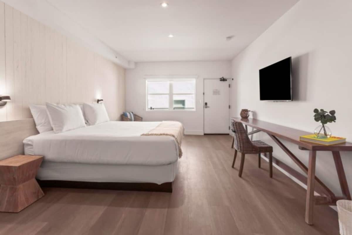 Un dormitorio moderno con cama, mesita de noche, silla y televisor montado en la pared.