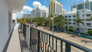 A balcony with a view of a city street, buildings, and palm trees. - Casa SOBE (Miami Beach)