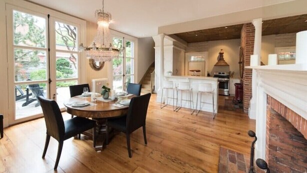 A dining area with a wooden table and chairs, a chandelier, and a view of the kitchen and outdoor patio. - Capitan Burn's House on Wellington
 (Kingston)
