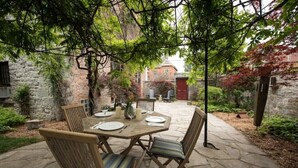 An outdoor patio with a stone table set for dining, surrounded by wicker chairs with cushions. - Capitan Burn's House on Wellington
 (Kingston)