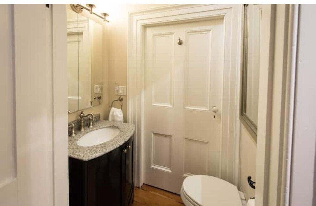 A bathroom with a white toilet, a sink with a granite countertop, and a mirror above the sink.