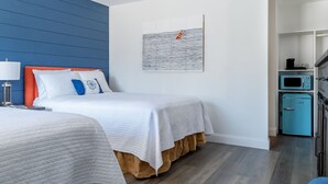 A hotel room with a bed, a nightstand, a lamp, a painting, a microwave, and a small cabinet.