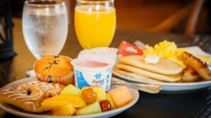A breakfast plate with pancakes, eggs, sausage, and a variety of fruits and a muffin.