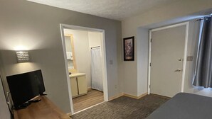A hotel room with a bed, a wooden desk with a television, a bathroom with a shower curtain, and a small kitchenette. - Endless Mountain Resort (Union Dale)