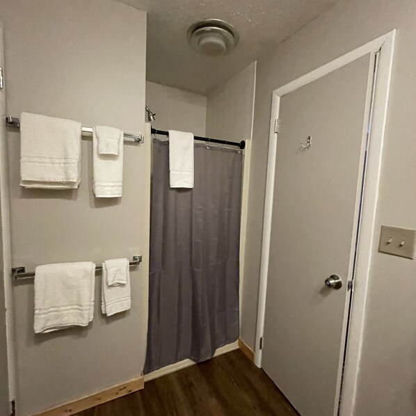 A bathroom with a shower curtain, a towel rack with multiple towels, and a door with a lock.