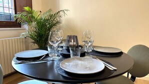 Ein Esstisch ist gedeckt mit Tellern, Gläsern und Besteck, umgeben von Stühlen und einem Blumentopf.
