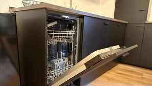 Eine moderne Küche mit integriertem Geschirrspüler, Holzboden und dunklen Schränken.