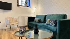 Ein Wohnzimmer mit einem grünen Sofa, einem weißen Sessel, einem Glastisch und einem kleinen Tisch mit einer Kerze.