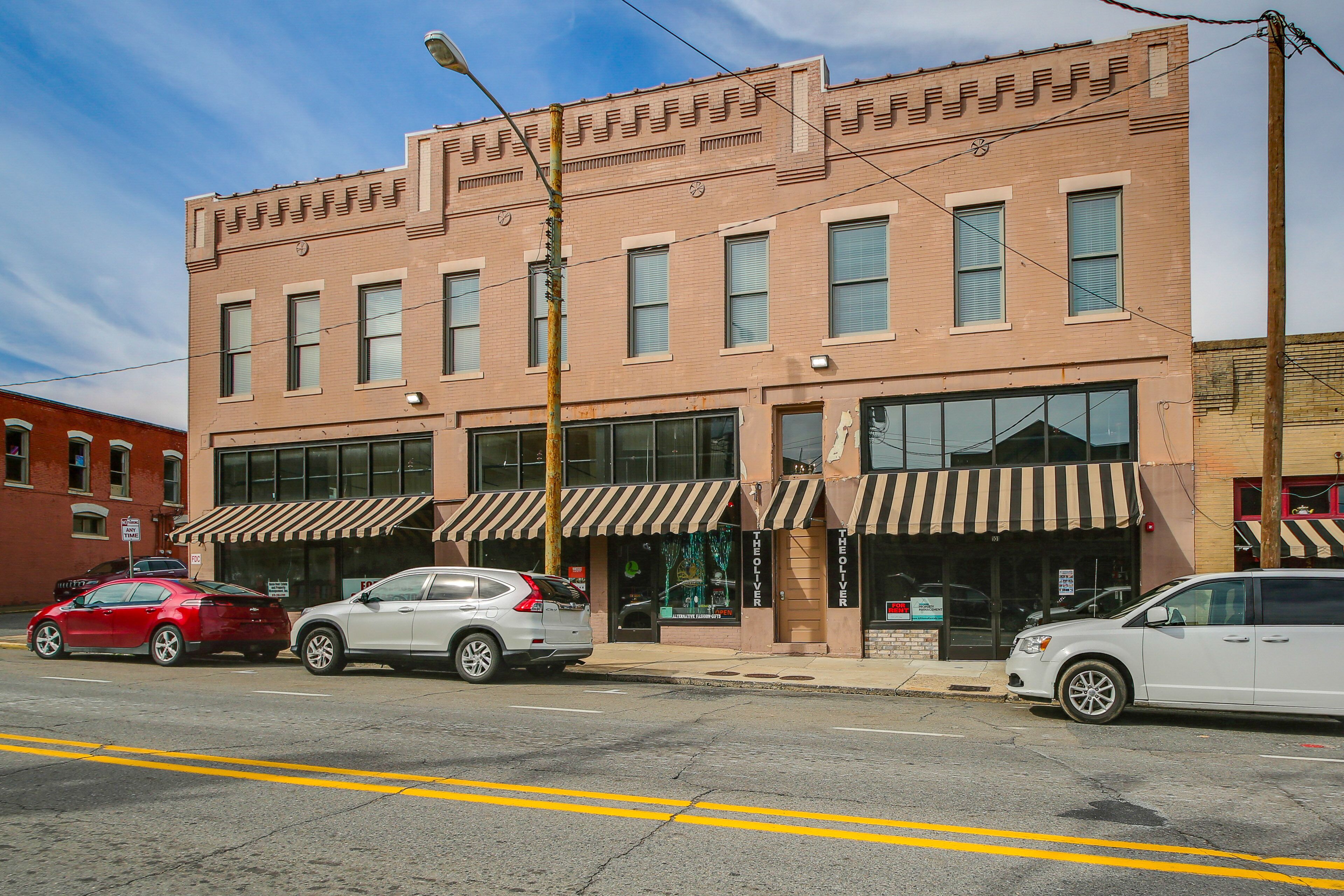 A two-story building with a brick facade, storefronts with awnings, and parked cars along the street.