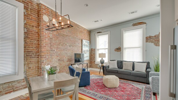 A living room with a brick wall, a dining table with chairs, a sofa, and a patterned rug. - Downtown Hot Springs Condo Near Bathhouse Row! (Hot Springs)