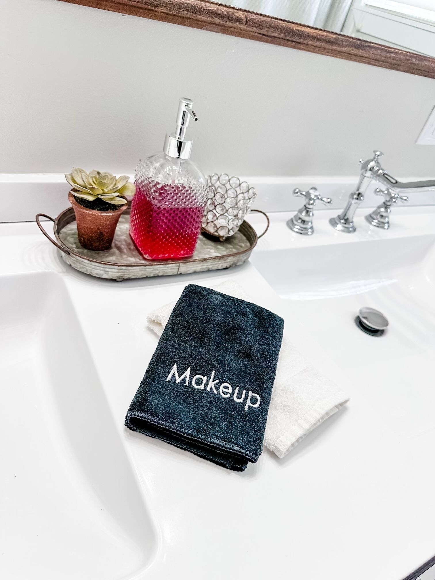 Un lavabo de salle de bain avec une serviette pour se maquiller, une plante en pot et des objets décoratifs.