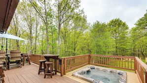 Een houten terras met een jacuzzi, tuinmeubilair en uitzicht op een bos.