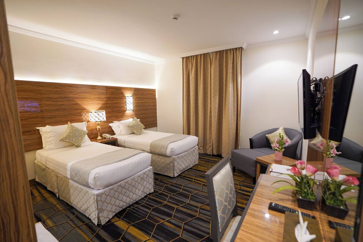 A hotel room with two beds, a TV, a desk, and a chair.