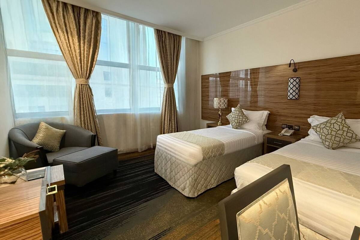 A hotel room with two beds, a sofa, a desk, and a window with curtains.