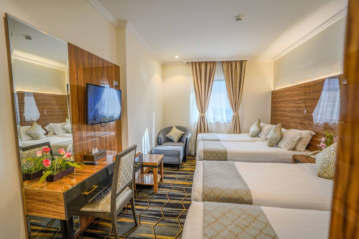 A hotel room with a desk, two beds, a TV, and a large mirror.