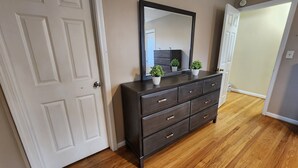 Een donkerhouten dressoir met spiegel, twee kleine planten in potten, en een witte deur met zilveren deurklink.