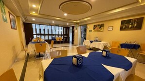Une salle à manger d’hôtel avec des tables dressées pour le service, une grande fenêtre laissant entrer la lumière naturelle et une vue sur l’extérieur.
