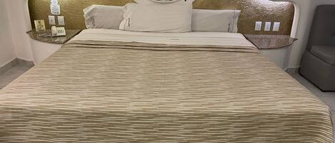 A hotel room with a large bed, a round mirror above the bed, a bedside table with a phone, and a chair.