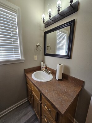 A bathroom with a white sink, wooden vanity, a large mirror, and a window with blinds. - Papas Cabin- block away from lake & Lacys marina. Property has Rv & boat parking (Higden)