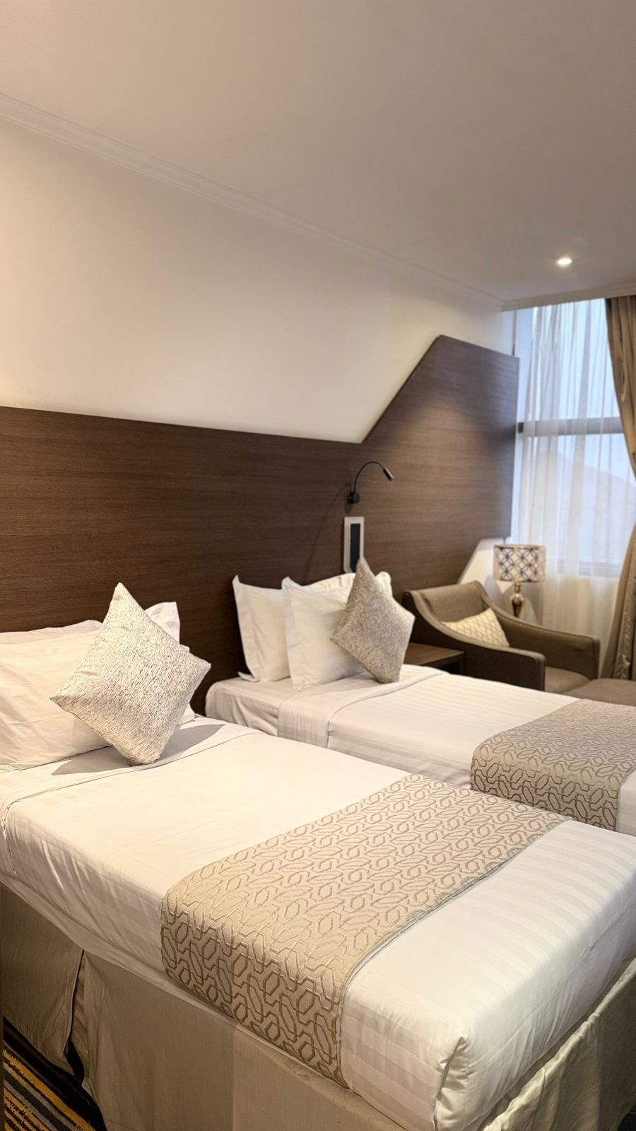 A hotel room with two beds, a nightstand, a chair, and a window with curtains.