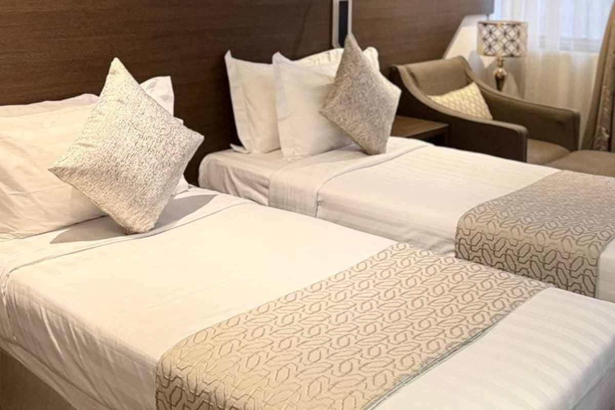 A hotel room with two beds, a nightstand, a chair, and a window with curtains.