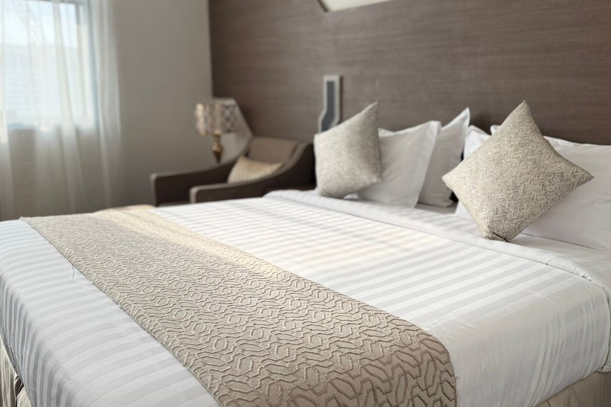 A hotel room with a large bed, a nightstand, a lamp, and a chair.