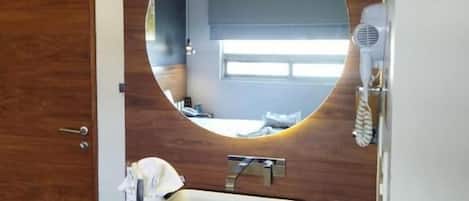 A bathroom with a round mirror, a sink, a hairdryer, and a towel on the counter.
