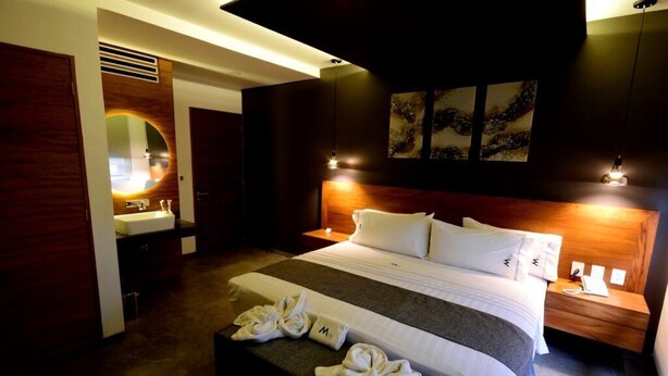 Een moderne hotelkamer met een groot bed, een nachtkastje met lamp, een spiegel en kunst aan de muur.