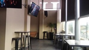 Een restaurant met hoge tafels en stoelen, een aan de muur bevestigde televisie en een groot raam met uitzicht.