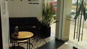 Een hotel receptie met een zwarte bank, een kleine ronde tafel en een potplant.