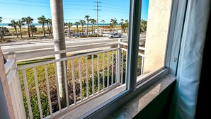 A balcony with a view of a beach, palm trees, and a road with vehicles. - Good Vibrations- Stay right ON the beach in Siesta Key! Sleeps 6 (Siesta Key)