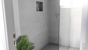 Un baño moderno con cabina de ducha de vidrio, paredes con azulejos blancos y una planta en maceta.