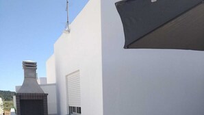 Una terraza en la azotea con una parrilla incorporada, paredes blancas y una mesa con sillas.