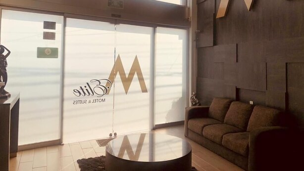 A modern interior with a large sliding door marked with a logo, a round glass table, and a brown sofa. - HOTEL M DORADO (Mexico City)